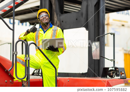 African male dock worker control loading containers cargo at warehouse container shipyard. Marine and carrier staff employee. cargo loading operator shipping export logistics ship yard. African male dock worker control loading containers cargo at warehouse container shipyard. Marine and carrier staff employee. cargo loading operator shipping export logistics ship yard. 107595882