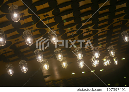 Upper view of the ceiling is decorated with yellow circle light bulbs in a modern style in Shopping Center Upper view of the ceiling is decorated with yellow circle light bulbs in a modern style in Shopping Center 107597491