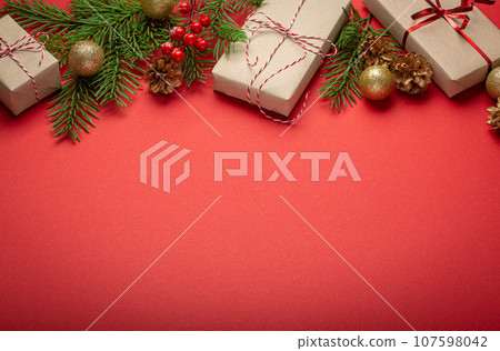 Christmas or New Year celebration red paper festive background with decoration fir tree, wrapped present boxes, cones, berries, sparkly red balls. Space for text. 107598042