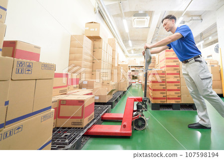 A man working in a warehouse using a hand lift 107598194