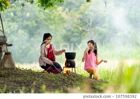 Close up Asian woman look like mother hold and prepare to cook rice near rice field and her daughter 107598392