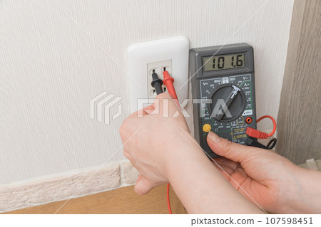 [Housewife measuring outlet voltage with a tester] 107598451