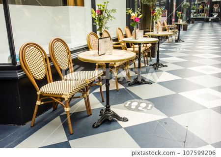 Wooden chairs, tables, and flowers placed in front of a cafe in an arcade in Cardiff, Wales Wooden chairs, tables, and flowers placed in front of a cafe in an arcade in Cardiff, Wales 107599206