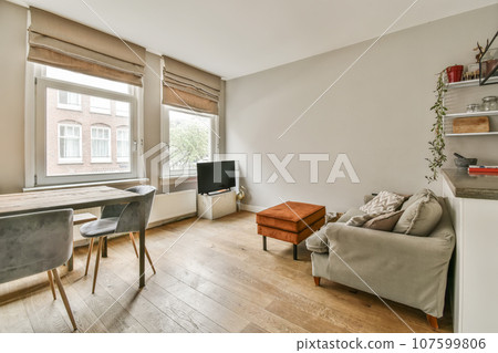 a living room with wood flooring and white walls, there is a small dining table in front of the window 107599806