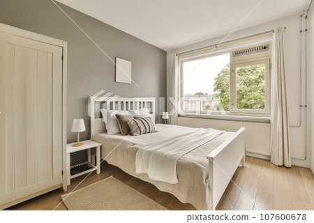 a bedroom with grey walls and hardwood flooring, white bed in the room has a large window overlooking out onto the street 107600678
