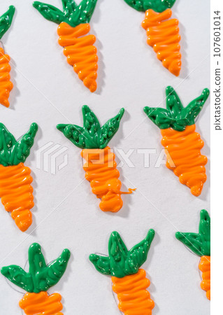 Piping melted chocolate from a piping bag over the parchment paper to make chocolate carrot cake toppers. 107601014