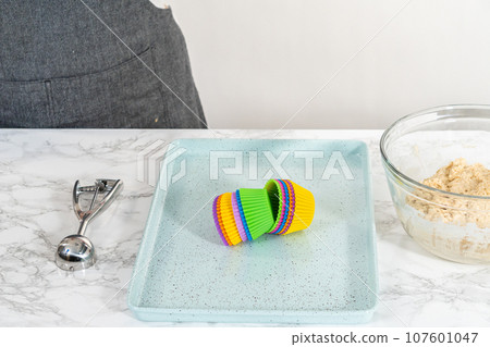 Scooping cupcake batter with dough scoop into silicon muffin liners to lemon poppy seed muffins. 107601047