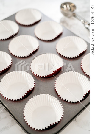 Scooping cake batter with dough scoop into cupcake foil liners to bake chocolate peppermint cupcakes. 107601145