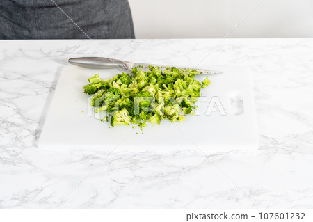 Chopping freshly steamed broccoli on a white cutting board. 107601232