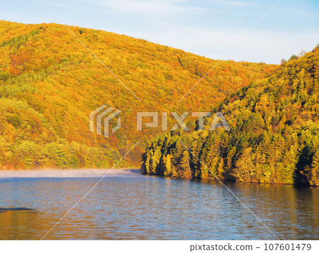 mountainous autumn landscape with lake. nature background with trees on the shore in fall colors. warm sunny weather. scenery in morning light mountainous autumn landscape with lake. nature background with trees on the shore in fall colors. warm sunny weather. scenery in morning light 107601479