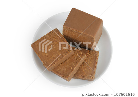 Brown cheese. Norwegian brunost in a ceramic bowl isolated on white background. Top view. Flat lay Brown cheese. Norwegian brunost in a ceramic bowl isolated on white background. Top view. Flat lay 107601616