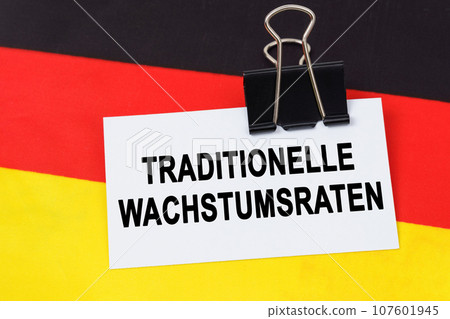 Economy and finance concept. On the flag of Germany lies a business card with the inscription - traditional growth rates. Text in German. Economy and finance concept. On the flag of Germany lies a business card with the inscription - traditional growth rates. Text in German. 107601945