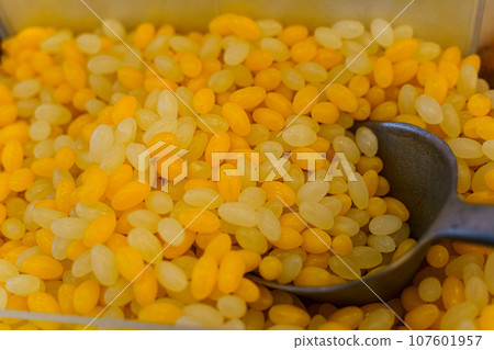 There are yellow and orange gummies and a scoop on the counter. Candy store. 107601957