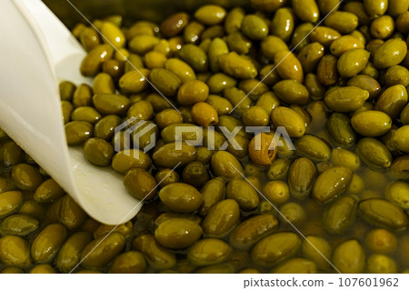 Seasoned olives with marinade and a white spatula in a container on the counter. Close-up. 107601962