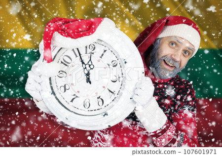 Santa Claus holds a clock in his hands, on which 5 minutes are left until the new year, Christmas, against the background of the flag of Lithuania. New year and christmas concept. Santa Claus holds a clock in his hands, on which 5 minutes are left until the new year, Christmas, against the background of the flag of Lithuania. New year and christmas concept. 107601971