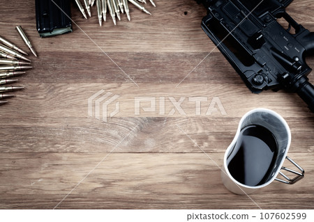 assault rifle and cup of coffee on wooden table assault rifle and cup of coffee on wooden table 107602599