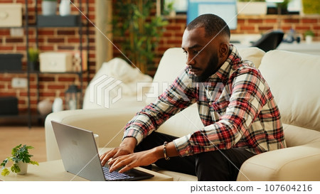 Remote worker solving job tasks in cozy modern apartment personal office. Freelancer teleworking from home, typing on keyboard and smiling at camera, slow motion close up 107604216