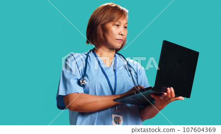 Close up shot of experienced healthcare expert imputing patient data on laptop after finishing clinical checkup appointment. Nurse typing informations on notebook, isolated over studio background Close up shot of experienced healthcare expert imputing patient data on laptop after finishing clinical checkup appointment. Nurse typing informations on notebook, isolated over studio background 107604369