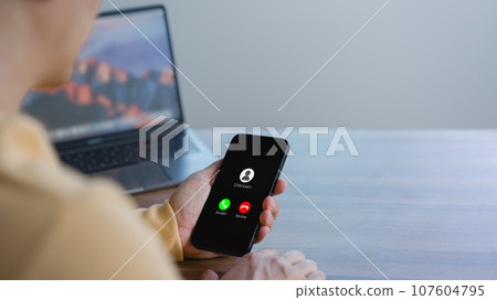 Guy answering the incoming call. The phone call was from an unknown number. Call center gang or stranger. Hoax person with a fake identity. Concept of scam, fraud with smartphone from the criminal. 107604795