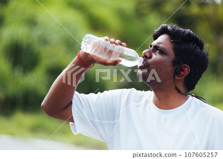Close up Asian young sport runner black man wear athlete headphones he drinking water from a bottle after running at the outdoor street health park, healthy exercise workout concept Close up Asian young sport runner black man wear athlete headphones he drinking water from a bottle after running at the outdoor street health park, healthy exercise workout concept 107605257