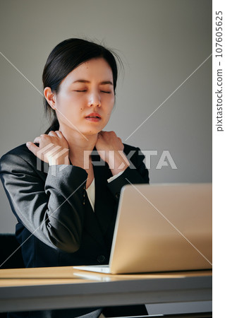 A young woman with stiff shoulders working at a desk 107605625