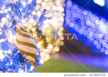 Blue golden glittering baubles xmas ornament ball decorated on christmas tree. Seasonal holiday winter xmas happy new year festival celebration. Blurred background Light gold ball Blue Christmas tree Blue golden glittering baubles xmas ornament ball decorated on christmas tree. Seasonal holiday winter xmas happy new year festival celebration. Blurred background Light gold ball Blue Christmas tree 107605720
