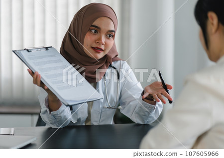 Young muslim female doctor in brown hijab headscarf having appointment consulting female patient in modern clinic hospital. Medical healthcare concept. 107605966