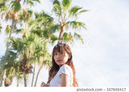 A woman basking in the sunset with palm trees in the background A woman basking in the sunset with palm trees in the background 107608417