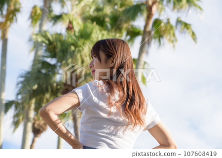A woman basking in the sunset with palm trees in the background A woman basking in the sunset with palm trees in the background 107608419
