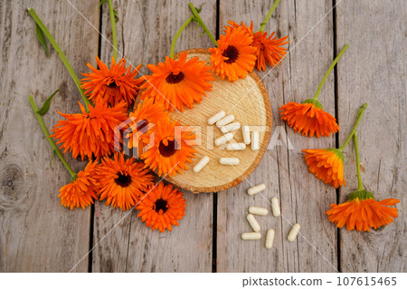 Calendula alternative medicine. White pills on a wooden table, fresh blooming calendula background. Flat lay Calendula alternative medicine. White pills on a wooden table, fresh blooming calendula background. Flat lay 107615465