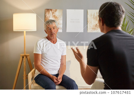 Senior man white T-shirt talking to psychologist at mental health, mature male talking with his son posing backwards about home problems family conflict. Senior man white T-shirt talking to psychologist at mental health, mature male talking with his son posing backwards about home problems family conflict. 107617481
