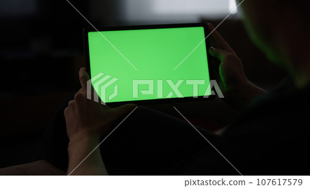 Man at home lying on a couch with tablet pc with green screen Man at home lying on a couch with tablet pc with green screen 107617579
