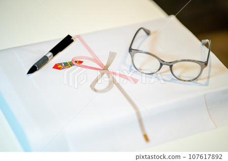 A pen and reading glasses are placed on top of the paper-covered items. A pen and reading glasses are placed on top of the paper-covered items. 107617892