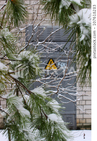 Snow Covered Pine Tree In Front Of Transformer Building With Metal Door And High Voltage Risk Sign 107618283