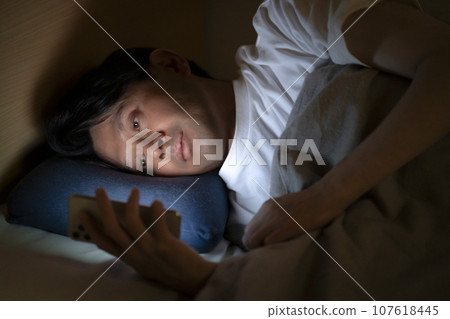 man using smartphone in bed 107618445