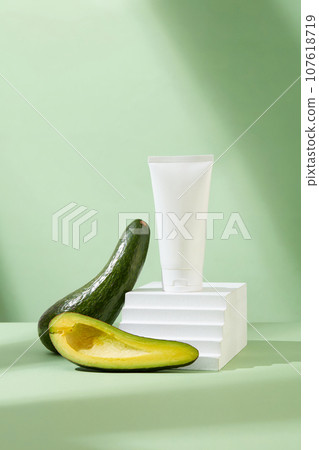 Minimalist concept for advertising cosmetic with natural extract. Fresh avocado decorated with cosmetics bottle on white stair podium on pastel green background. Front view 107618719