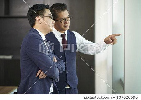two asian business men standing by office window having a discussion 107620596