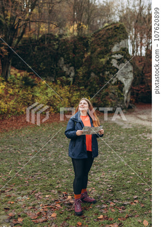 Positive cheerful girl holding paper map over nature background. Mountain peaks. Freedom, happiness, travel and vacations concept, outdoor activities, full body Positive cheerful girl holding paper map over nature background. Mountain peaks. Freedom, happiness, travel and vacations concept, outdoor activities, full body 107620899
