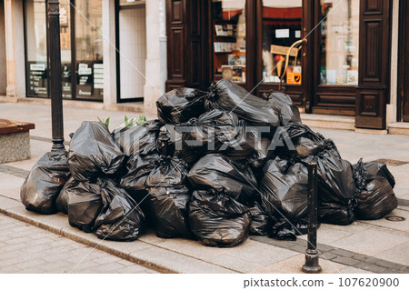 Pile of black garbage on the footpath at side road in big city, pollution trash. Many garbage plastic bags black waste, pollution, lots junk dump 107620900