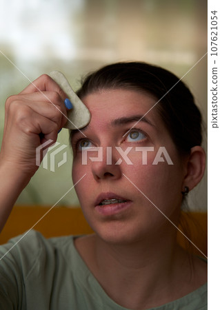 Woman is massaging her face scraper gua sha. 107621054