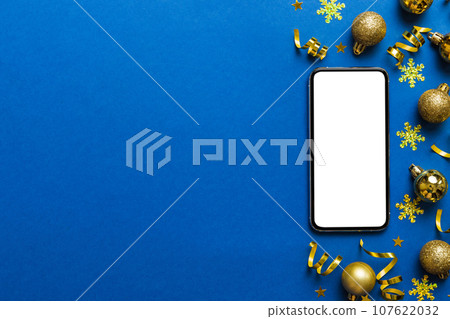 Christmas online shopping from home phone with blank white display top view. smart mobile with copy space on colored background with Christmas decorations balls,. Winter holidays sales background 107622032