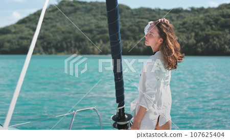 Woman in white shirt relaxes standing on yacht deck. Caucasian girl enjoys beautiful sea green island landscape. Travel, tourism, holiday yacht tour to Bora Bora islands. Slow motion 4K Woman in white shirt relaxes standing on yacht deck. Caucasian girl enjoys beautiful sea green island landscape. Travel, tourism, holiday yacht tour to Bora Bora islands. Slow motion 4K 107625404