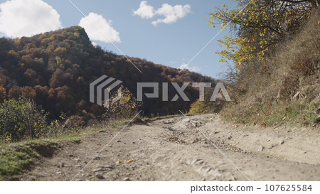 establishing shot on a dusty mountain road in autumn forest establishing shot on a dusty mountain road in autumn forest 107625584