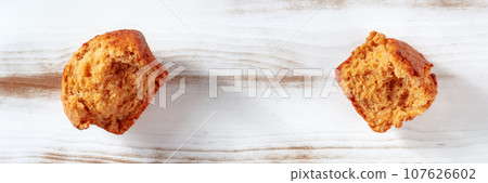 Broken orange muffin on a rustic wooden kitchen table panorama, top shot Broken orange muffin on a rustic wooden kitchen table panorama, top shot 107626602
