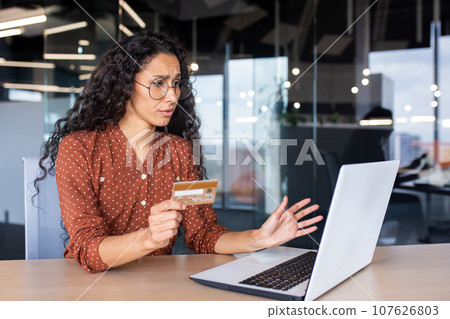 Upset and shocked business woman with bank credit card and laptop, female worker received rejection error at workplace inside office. 107626803