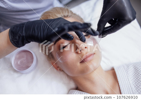 Close-up of a master applying silicone patches under the eyes of a pretty female blond client 107626910