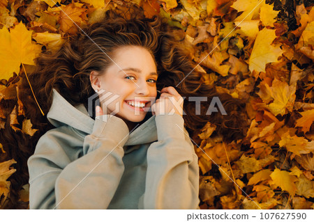 Smiling young woman lying on the autumn foliage in the forest with the yellow leaves 107627590