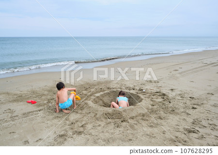 Children dig a hole in the sand on the seashore. Children dig a hole in the sand on the seashore. 107628295