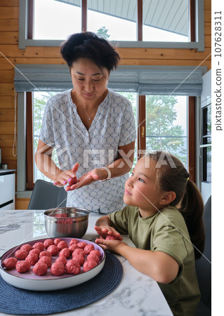 Grandmother and granddaughter preparing meatballs. Grandmother and granddaughter preparing meatballs. 107628311