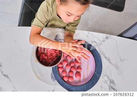 A girl is preparing meatballs in the kitchen. 107628312